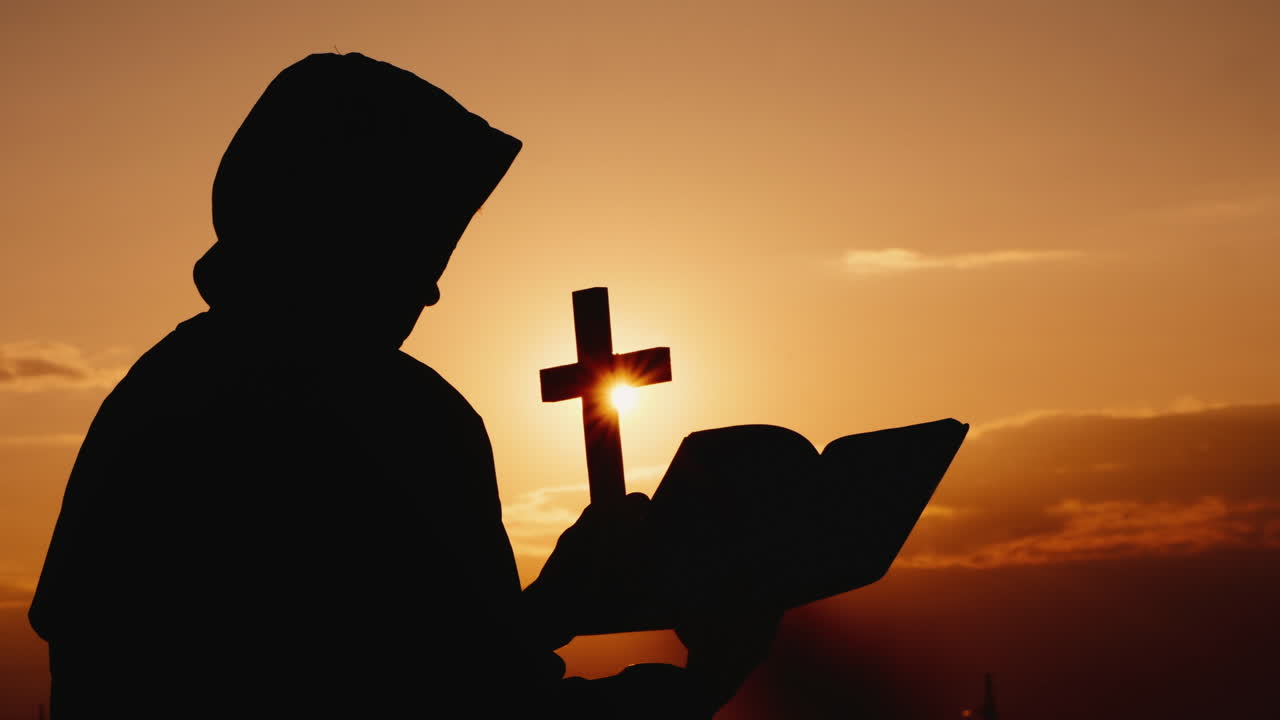 손에 십자가를 들고 두건을 쓴 승려가 극적인 일몰을 배경으로 서 있다