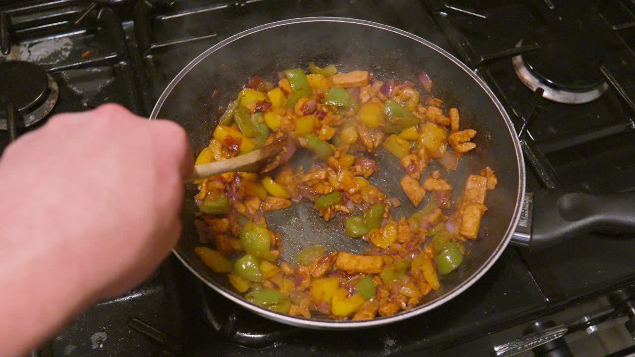 POV Point of View Cooking Spicy Mexican Fajita Mix with Chicken, Peppers, Onions on Gas Stove in Wok Ready to Load in Tortillas to Eat.
