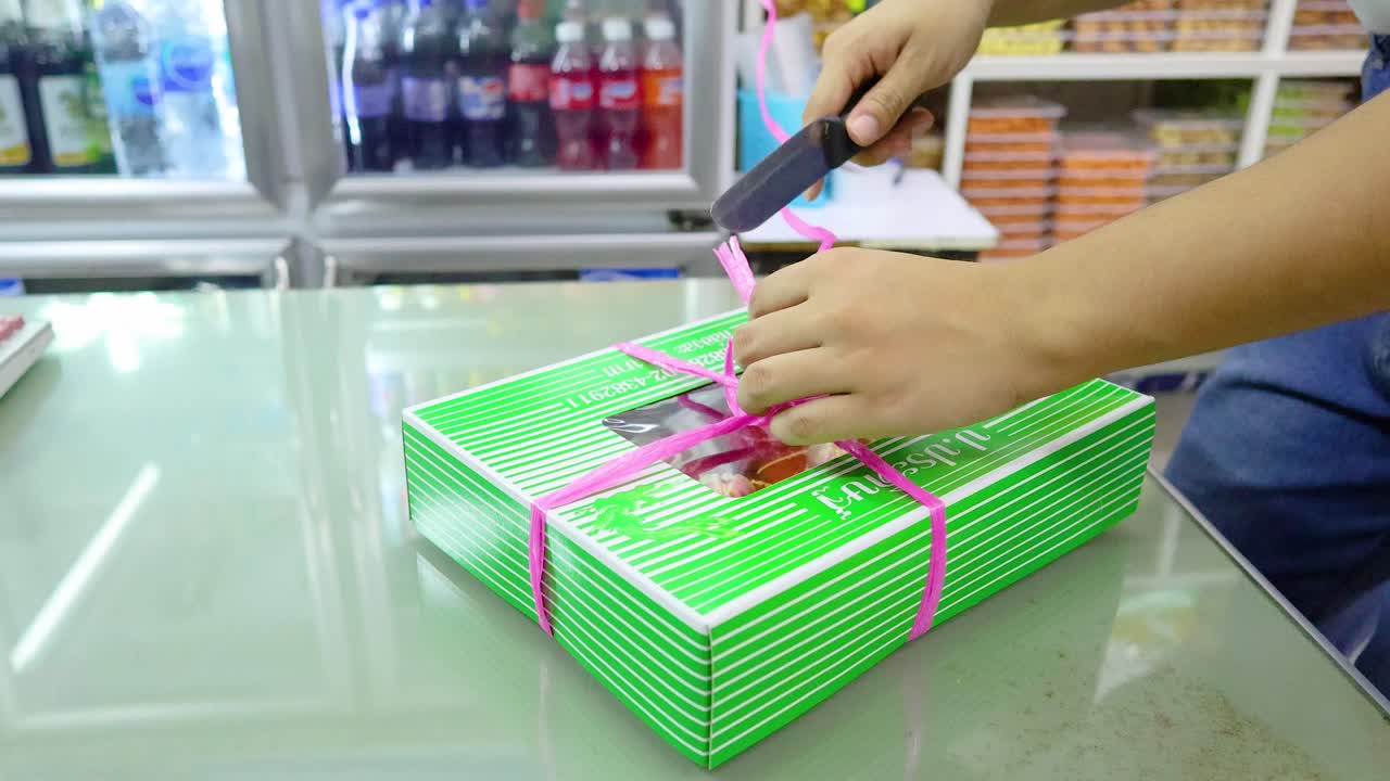 Hands untying a pink ribbon on a green gift box in a brightly lit store environment