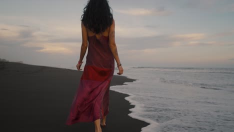 attractive woman in red dress walking in the beach with crashing waves