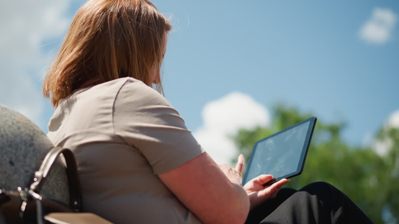 Woman turning phone around with empathy while looking at screen outdoors, wind gently moving hair, sunlight highlighting calm expression, serene atmosphere of connection