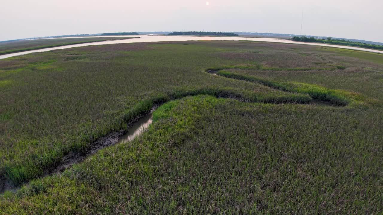 Aerial footage offers a sweeping view of dense South Carolina marshlands dotted by a narrow creek, leading toward the horizon beneath a calm sunrise sky