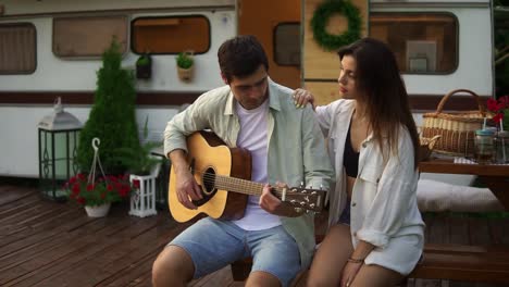 romantic couple sitting outdoors in front their home van and man playing the guitar for girlfriend. outdoor. girl listening music and hugging man