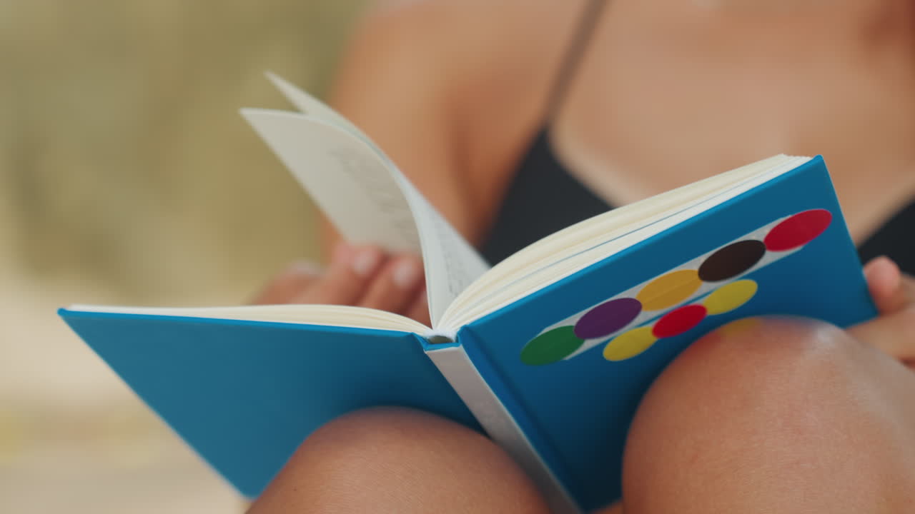 Donna in spiaggia che legge. Una donna con un quaderno colorato in spiaggia. Una donna rilassata che si gode una giornata di sole con un quaderno vivace. Scena casuale di una donna che legge un quaderno su una spiaggia assolata con una brezza leggera.