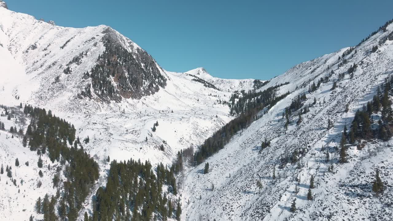 Luftaufnahme von schneebedeckten Berghängen und Nadelwald nahe dem Dorf Arshan, Republik Burjatien, Russland, mit klarem blauem Himmel und winterlicher Wildnis