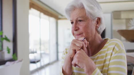 Thoughtful-senior-caucasian-woman-holding-pen-calculating-finances-sitting-at-home