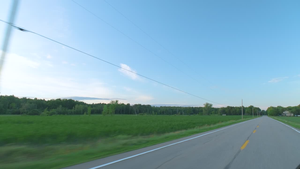 Shot from a car on a deserted rural road with beautiful a blue sky over a meadow field in Lanaudière, Québec