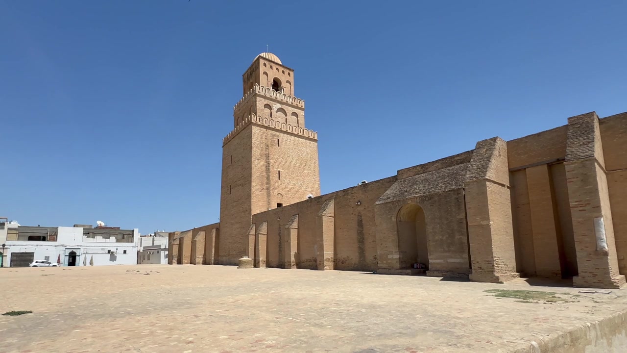 Ampia inquadratura diurna del minareto e delle mura esterne del cortile della Grande Moschea di Kairouan sotto un cielo azzurro e limpido, Tunisia.