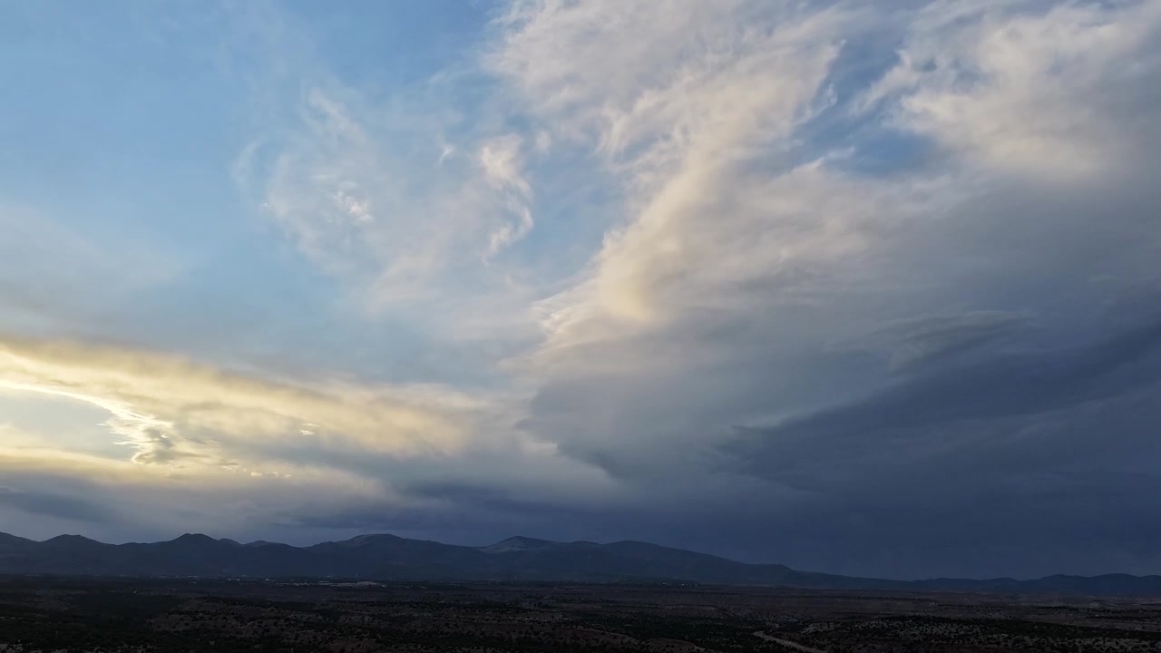 4K surreal drone timelapse captures varied cloud patterns over a vast desert landscape. Cinematic aerial motion reveals a striking beam of sunlight shining through a barrel of dual cloud layers.