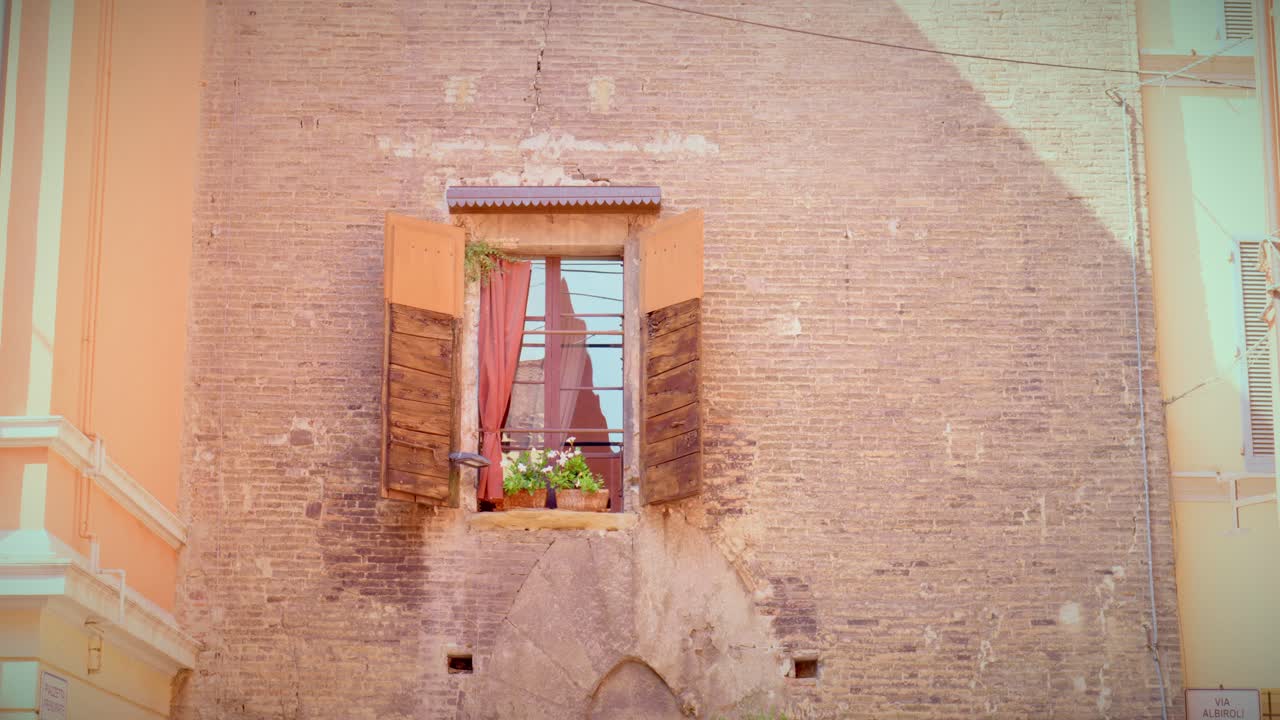Davanzale aperto con tende rosse e fiori in una fioriera, pareti texturizzate all'interno dello storico corridoio di Bologna