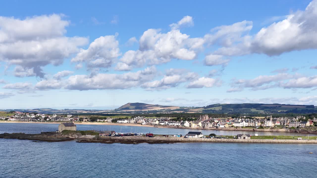 Daytime panoramic camera pan across Fife harbor, lighthouse, seaside village, hills, and blue sky