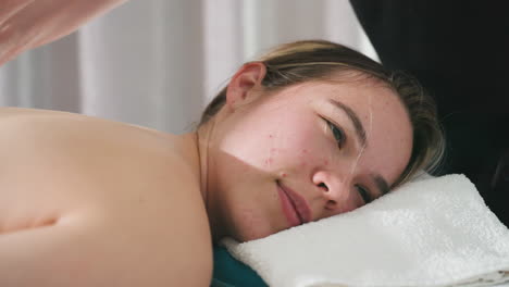 massage therapist gently glides smooth stone over client back while client rests head on soft white towel in serene spa setting with natural lighting, capturing peaceful relaxation