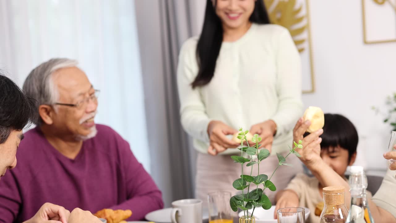 Three generations gather around a bright dining table, sharing food and conversation in a warmly lit, modern home environment with natural daylight