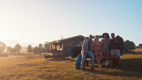 retrato de amigos sentados en la puerta trasera de una camioneta en un viaje por carretera a la cabaña en el campo