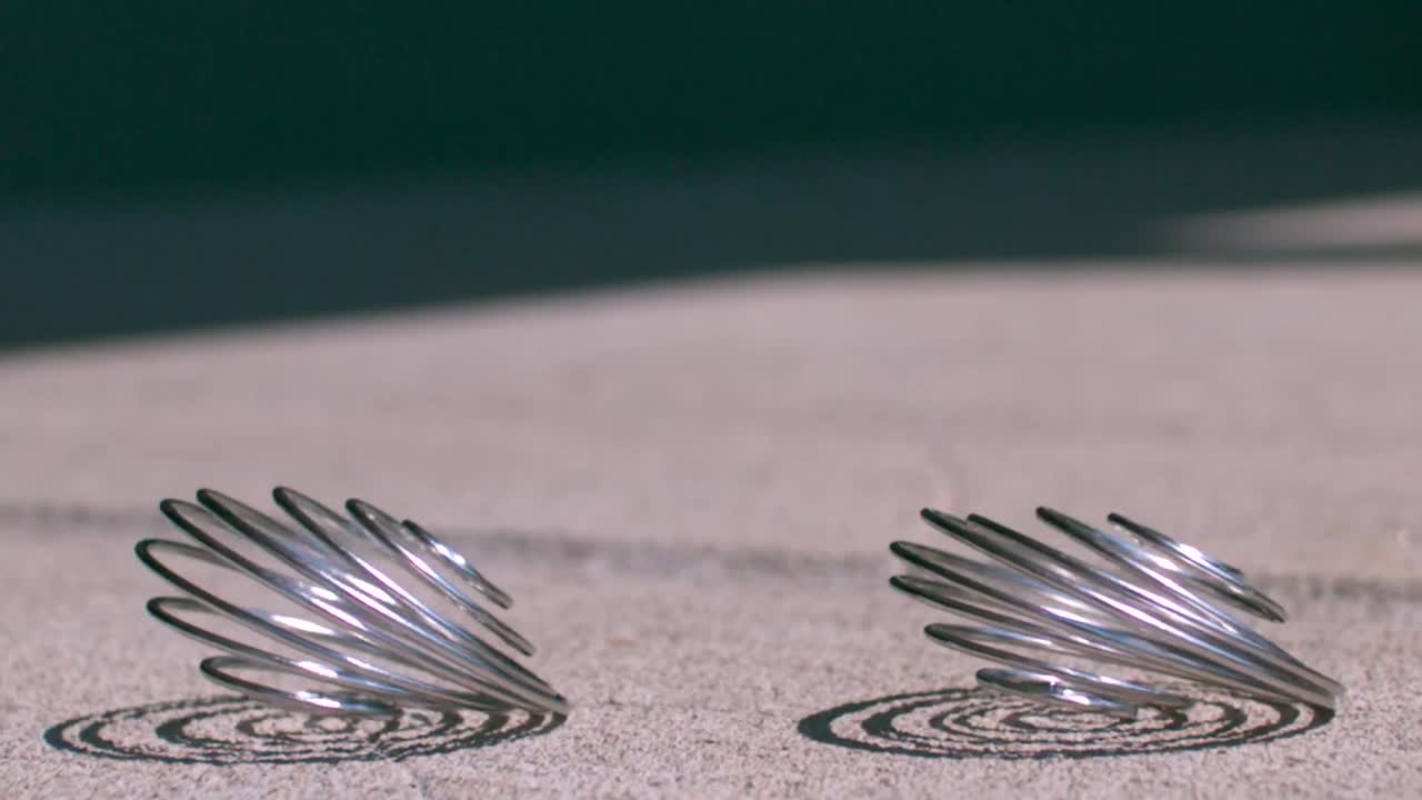 아스팔트 위에 떨어지는 금속 스프링은 빛이 비치는 여름날 동안 느린 동작으로 반사되어 영화적인 그림자를 만니다.