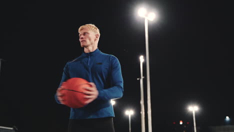 sportive blond man doing rotation core exercises using basketball in the park at night