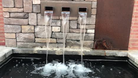 Close-up-of-water-flowing-from-wall-fountain-with-vintage-bricks-as-background