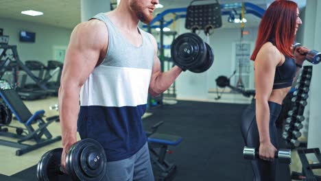 close-up of muscular man's body training together with athletic woman. young couple is training with dumbbells confidently in a modern gym.