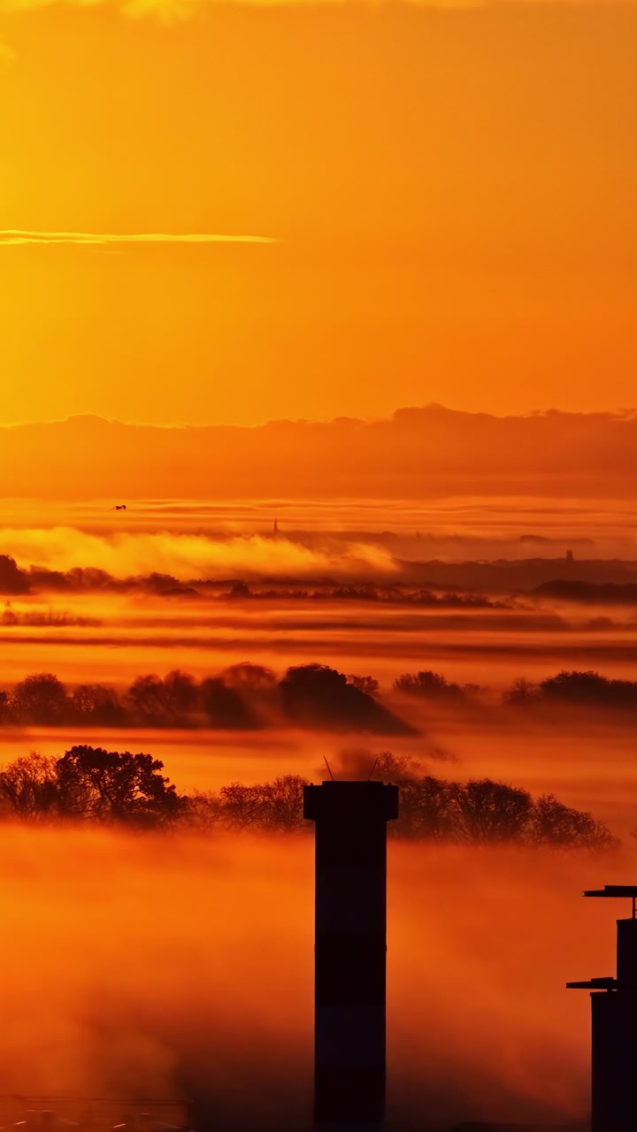 Silhouettierte Struktur vor intensivem orangefarbenem Sonnenuntergangslicht und atmosphärischem Dunst. Nützlich für Themen wie Sonnenuntergang, Landschaft, Energie, Umwelt und industrielle Infrastruktur, vertikale Luftaufnahme