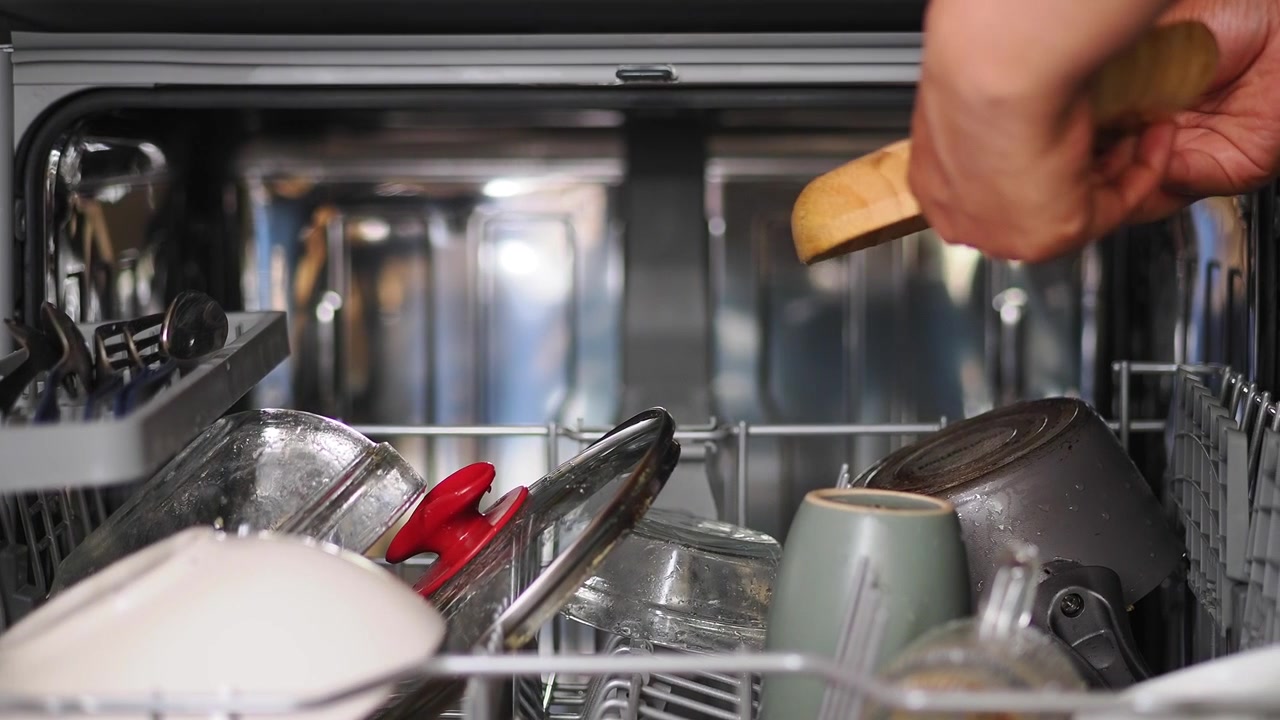 Person Organizing Dirty Dishes Inside a Dishwasher