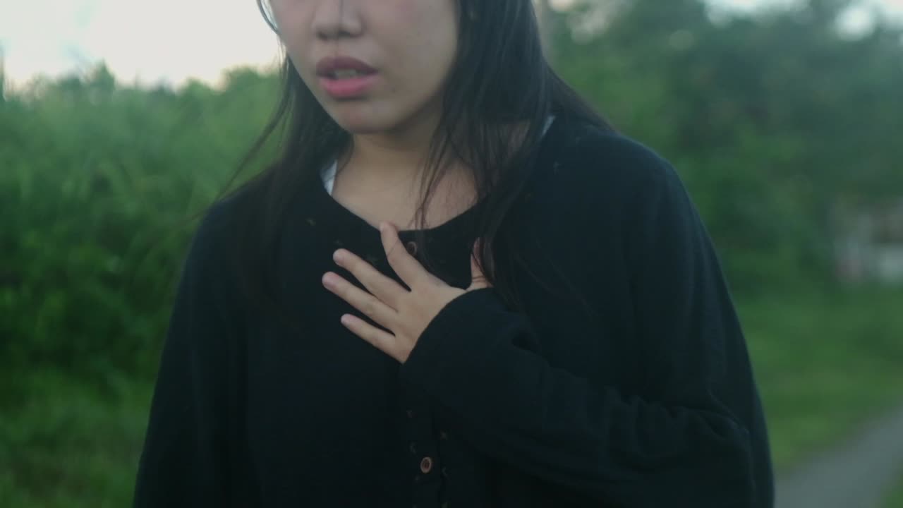 Slow-motion medium shot of a thoughtful, young woman with hand over chest walking in an outdoor setting.
