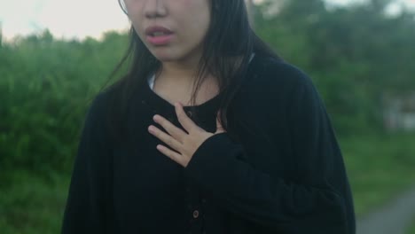 slow-motion medium shot of a thoughtful, young woman with hand over chest walking in an outdoor setting.