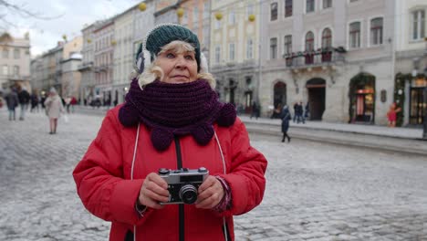 Senior-woman-tourist-taking-pictures-with-photo-camera,-using-retro-device-in-winter-city,-lockdown