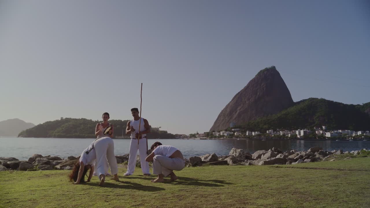 People practicing Capoeira by the water in Rio de Janeiro with Sugarloaf Mountain in the background
