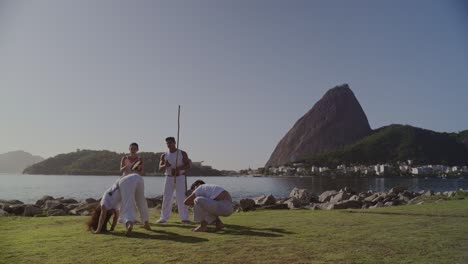 people practicing capoeira by the water in rio de janeiro with sugarloaf mountain in the background