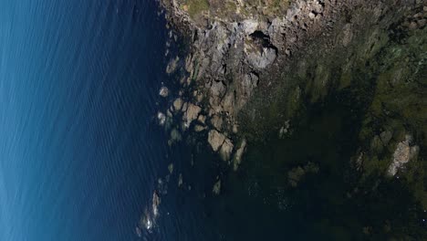 vertical video of sanxenxo coastline, tilt up from coastal rocks revealing peaceful seascape horizon, galiza