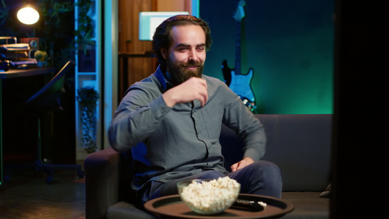 재는 코미디 영화를 보는 동안 소파에 앉아 웃는 행복한 남자