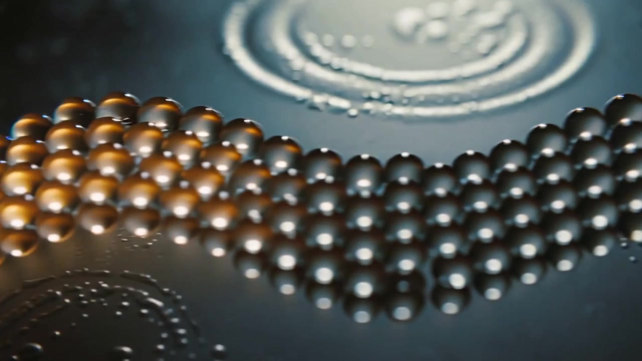 Catena di sfere lucide in movimento su un piatto scuro dopo un impatto liquido, con gocce e increspature