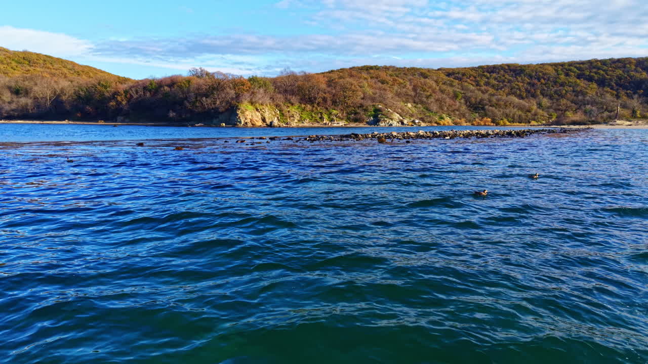 Ruhe auf dem Wasser, während sanfte Wellen an das Ufer in der Nähe einer zerklüfteten Küstenlinie unter einem strahlend blauen Himmel schlagen
