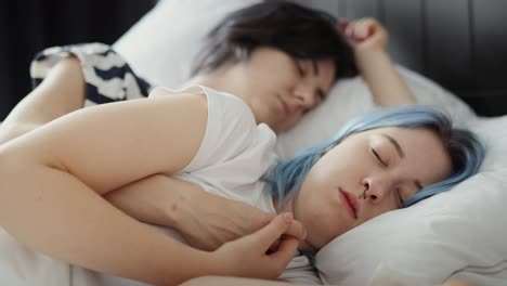 zoom out video of lesbian couple sleeping together in bed.