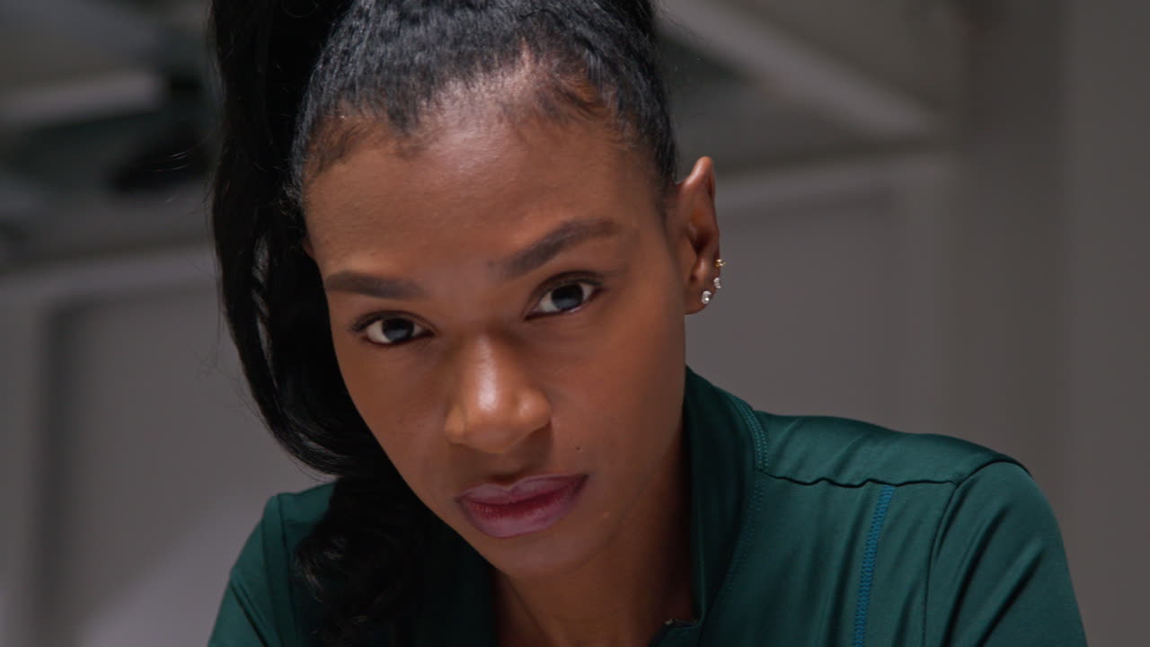 체육관에서 운동 훈련을 하고, 옷차림실에서 앉아서 집중하고, 집중된 표정으로 운동을 하는 여성 선수의 근접한 초상화.