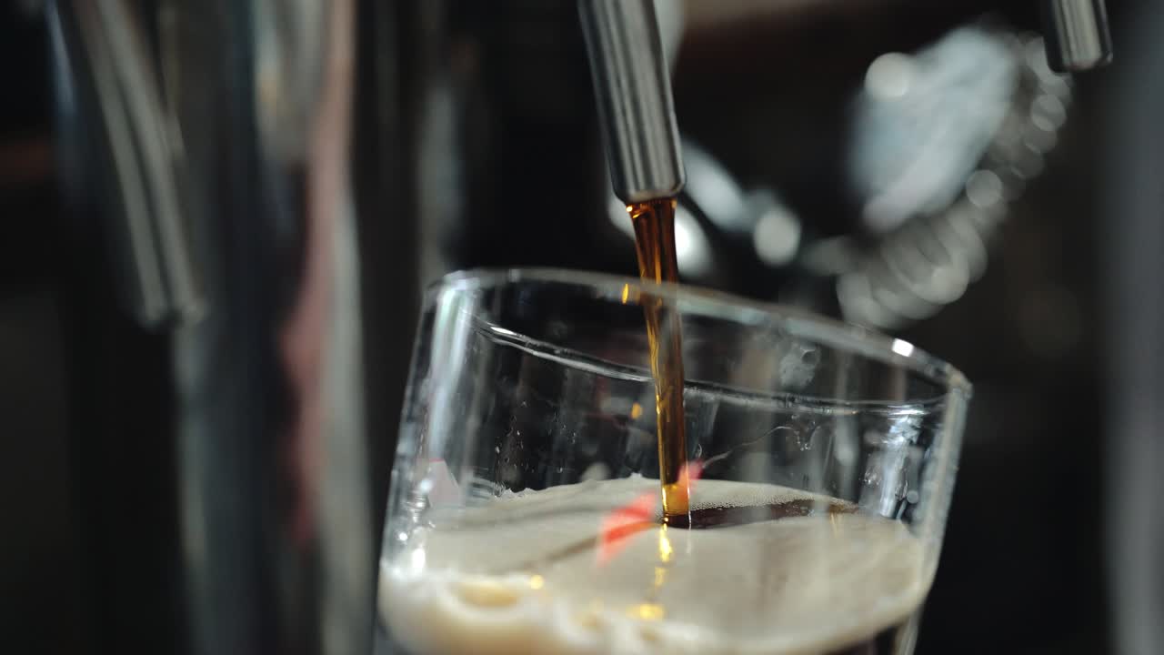 Bartender pours a dark beer in glass. Close-up.