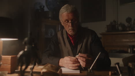 older passionate man evaluates an old silver skull watch in his office at night