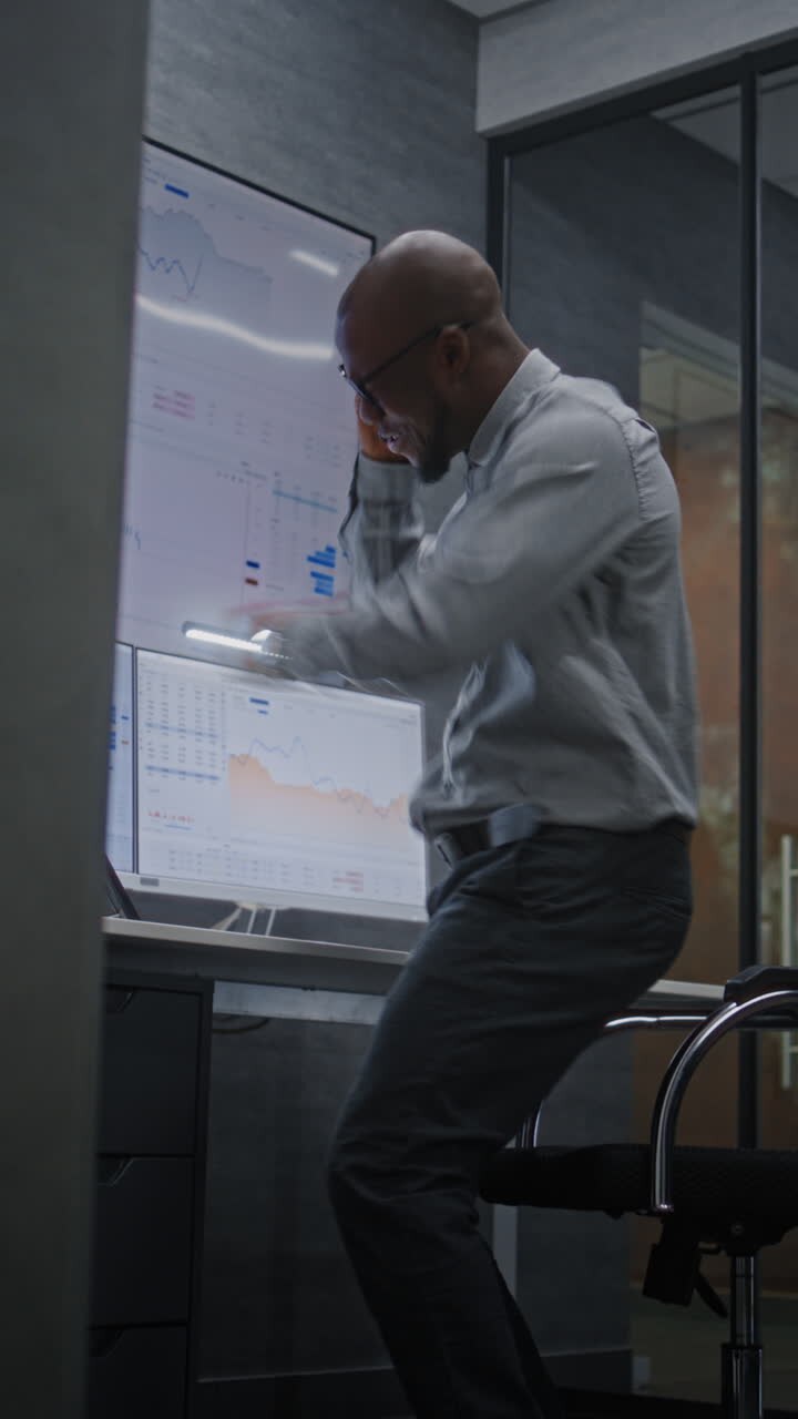 Happy African American Businessman in Advanced Trading Office: Excited Financial Analyst Jumping Celebrating Successful Financial Deal, Having Phone Call, Making Profitable Investments. Vertical Shot.