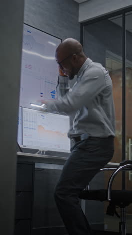 happy african american businessman in advanced trading office: excited financial analyst jumping celebrating successful financial deal, having phone call, making profitable investments. vertical shot.