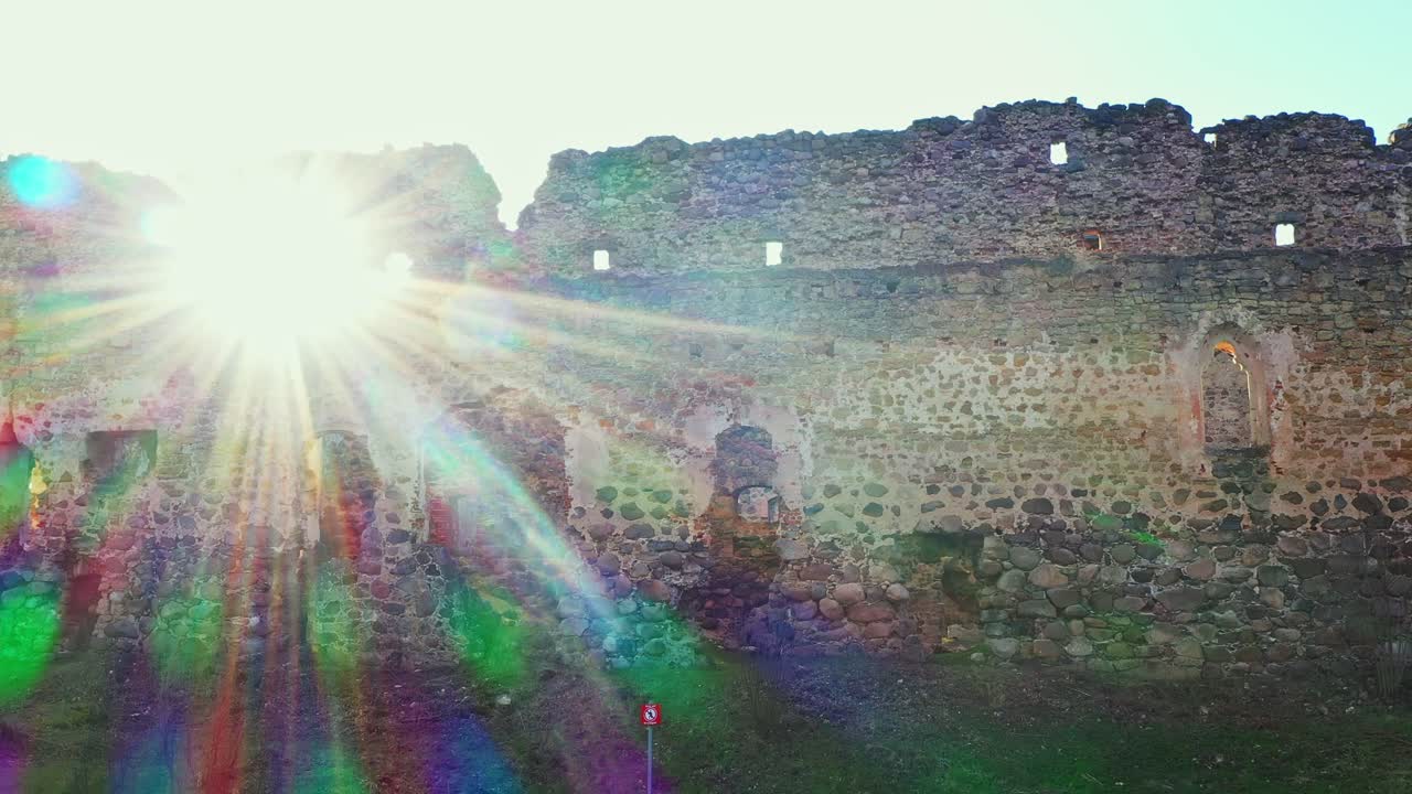 Aerial jib down shot of a wall of Rauna Castle and the sun shining through a hole