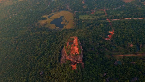 high-angle aerial drone footage directly above sigiriya rock fortress at sunrise, capturing the symmetrical design of the ancient ruins, surrounded by lush jungle and glowing morning mist.