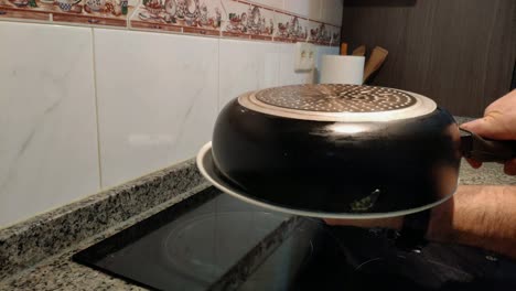 the hands of the cook using a plate to turn the spanish potato and egg omelette in the pan and finish cooking in electric hob cooker, shot blocked close-up, galicia, spain