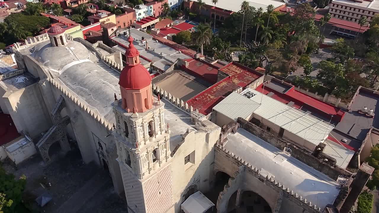 Drone View Flying Closer to a Historic Church in Cuernavaca, Capturing the Intricate Details of the Cross on the Church's Tower, Surrounded by Rich Architectural Elements and the Vibrant City Below