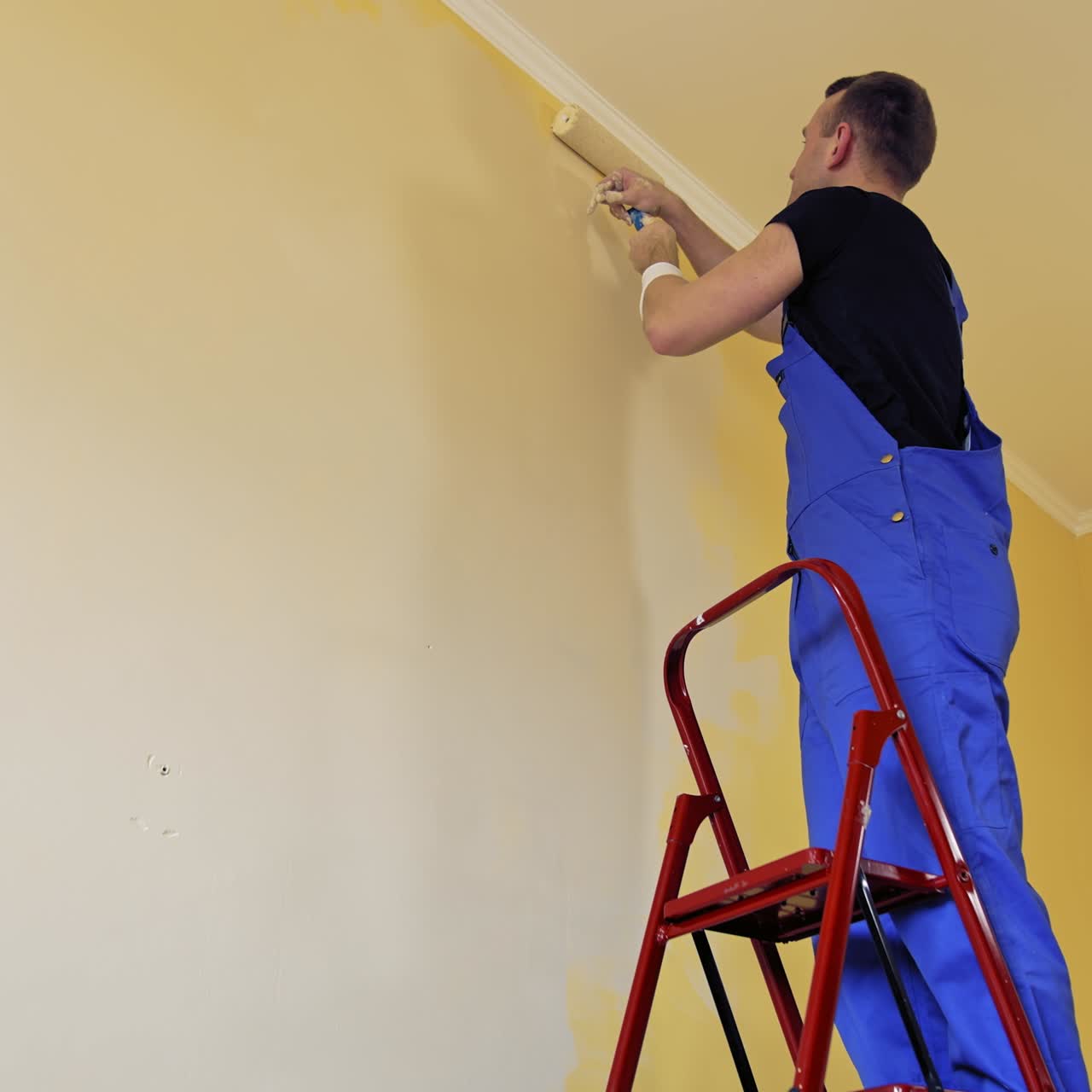 Man painting a yellow wall with a roller at work. Offering professional painting services