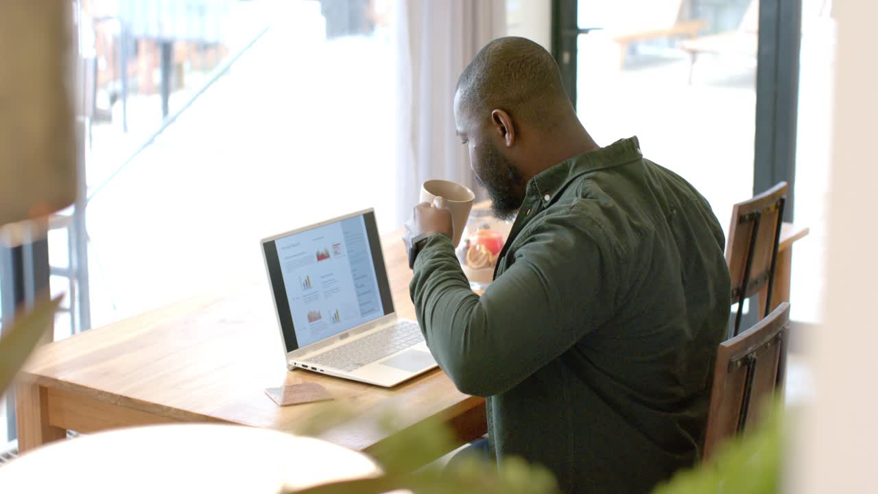 When reviewing laptop charts, man is pausing and sipping coffee from mug in cafe for focus