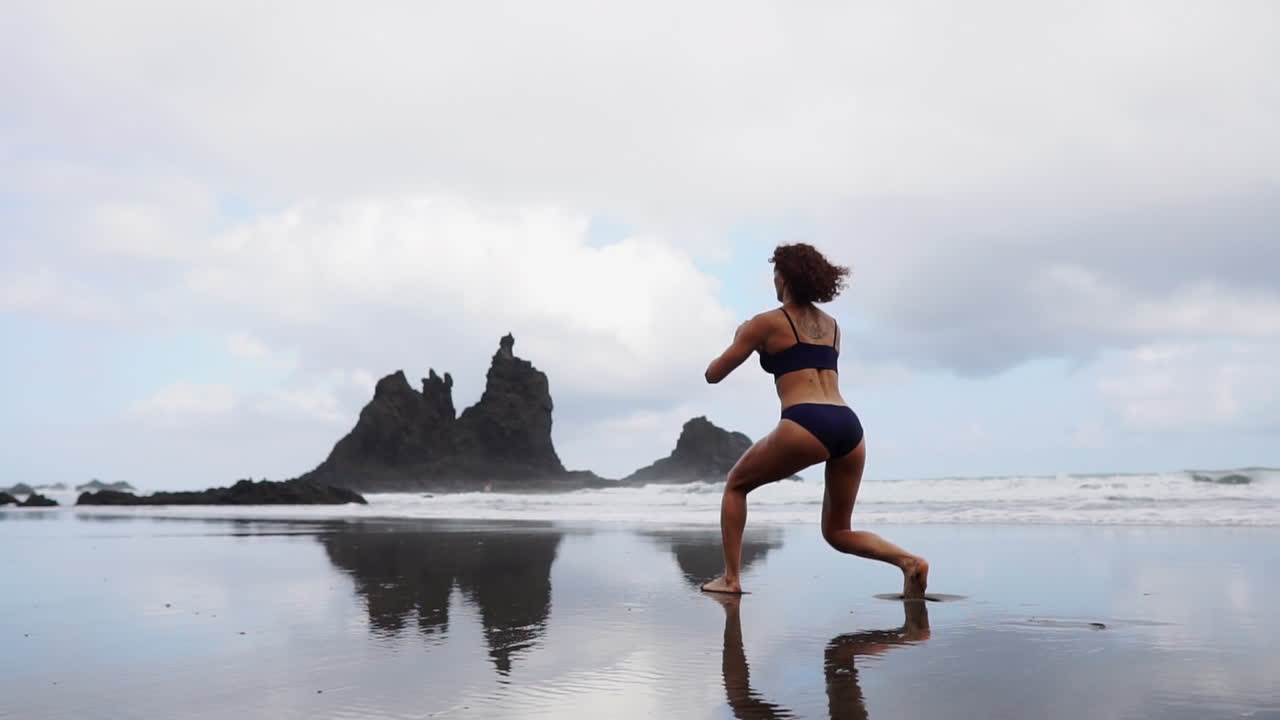 Slow motion captures a fitness woman stretching her legs or doing lunges on the beach, accompanied by a female athlete engaging in soothing exercises by the sea