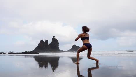 Cámara-Lenta-Captura-A-Una-Mujer-Fitness-Estirando-Las-Piernas-O-Haciendo-Estocadas-En-La-Playa,-Acompañada-Por-Una-Atleta-Realizando-Ejercicios-Relajantes-Junto-Al-Mar