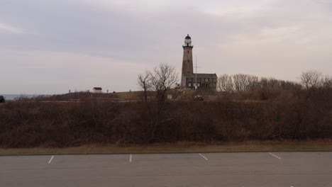 Eine-Drohnenansicht-Aus-Einem-Niedrigen-Winkel-Auf-Den-Leuchtturm-Von-Montauk-Während-Eines-Bewölkten-Sonnenuntergangs