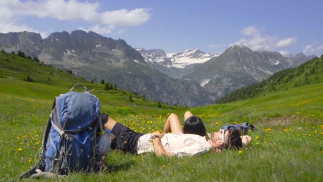 a woman rests with male partner on a hike through the mont blanc alps, surrounded by breathtaking views in wildflower meadow