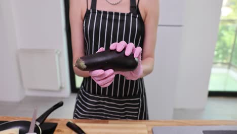 person in apron and pink gloves holding an eggplant